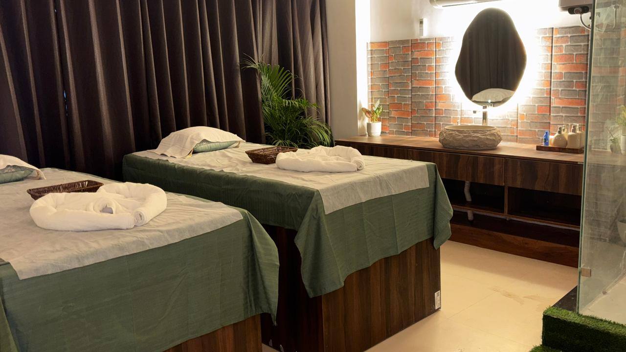 The couple room: two treatment beds side by side in green linen, brick wall and backlit mirror behind